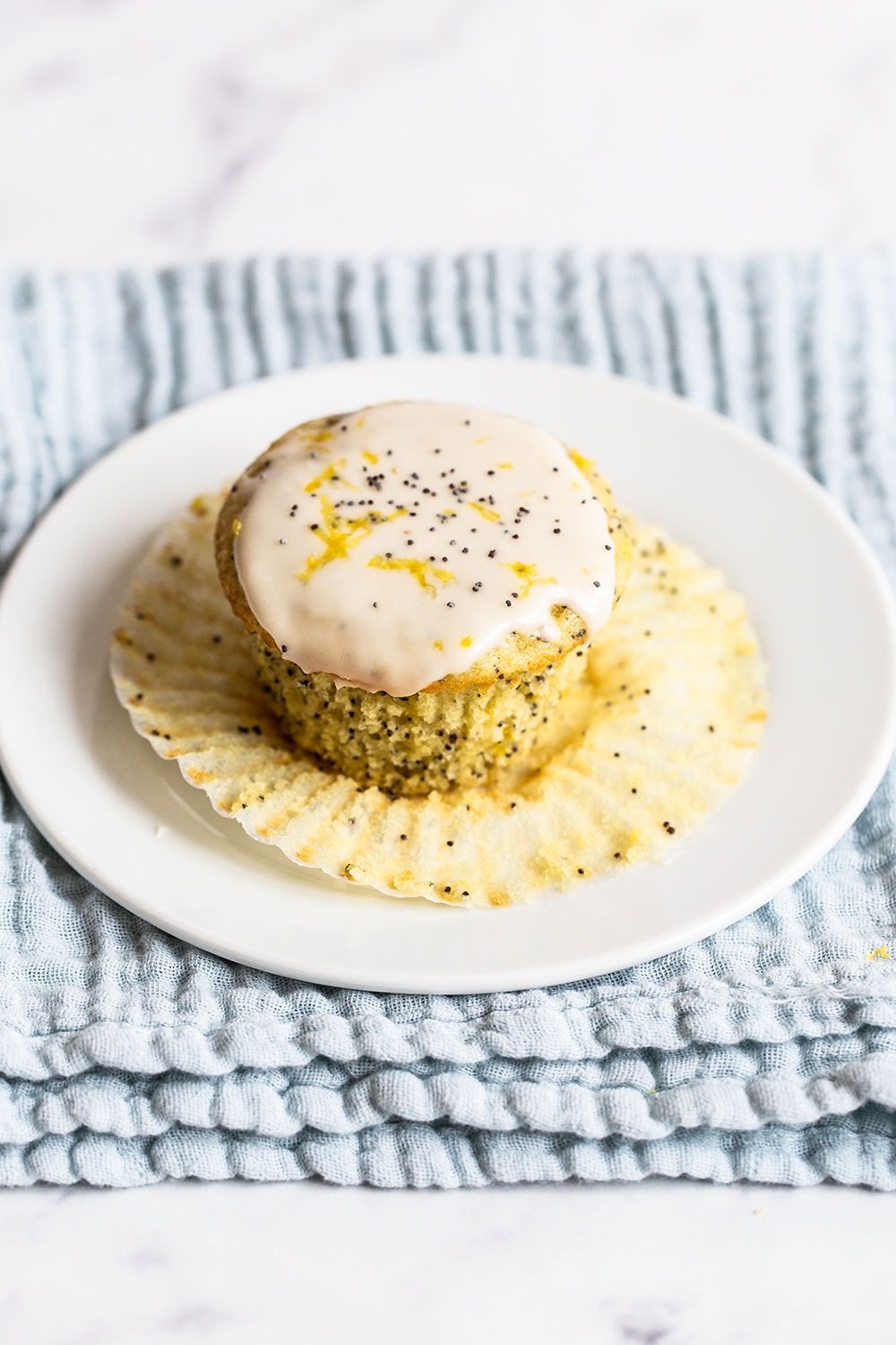 glazed lemon poppyseed muffin on a plate with the wrapper being removed