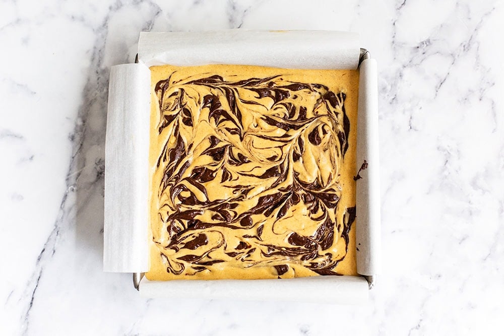 Chocolate cheesecake batter swirled into pumpkin batter and ready for the oven