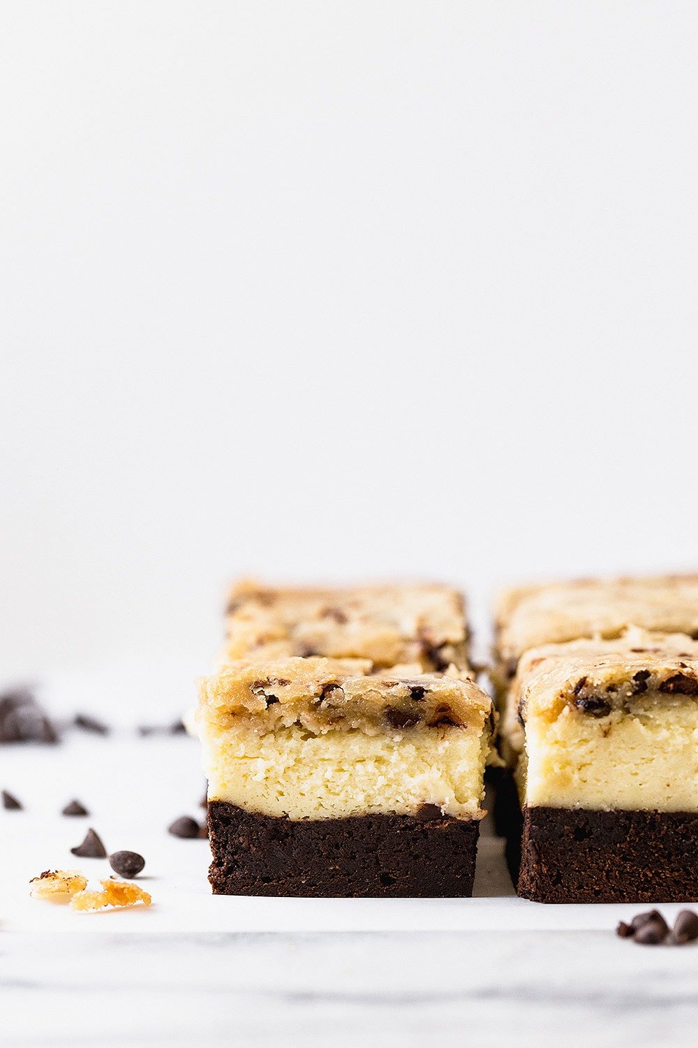Outrageous Brownie Bottom Cookie Dough Cheesecake Bars have a layer of fudgy brownie, cheesecake filling, and a chocolate chip cookie dough topping.