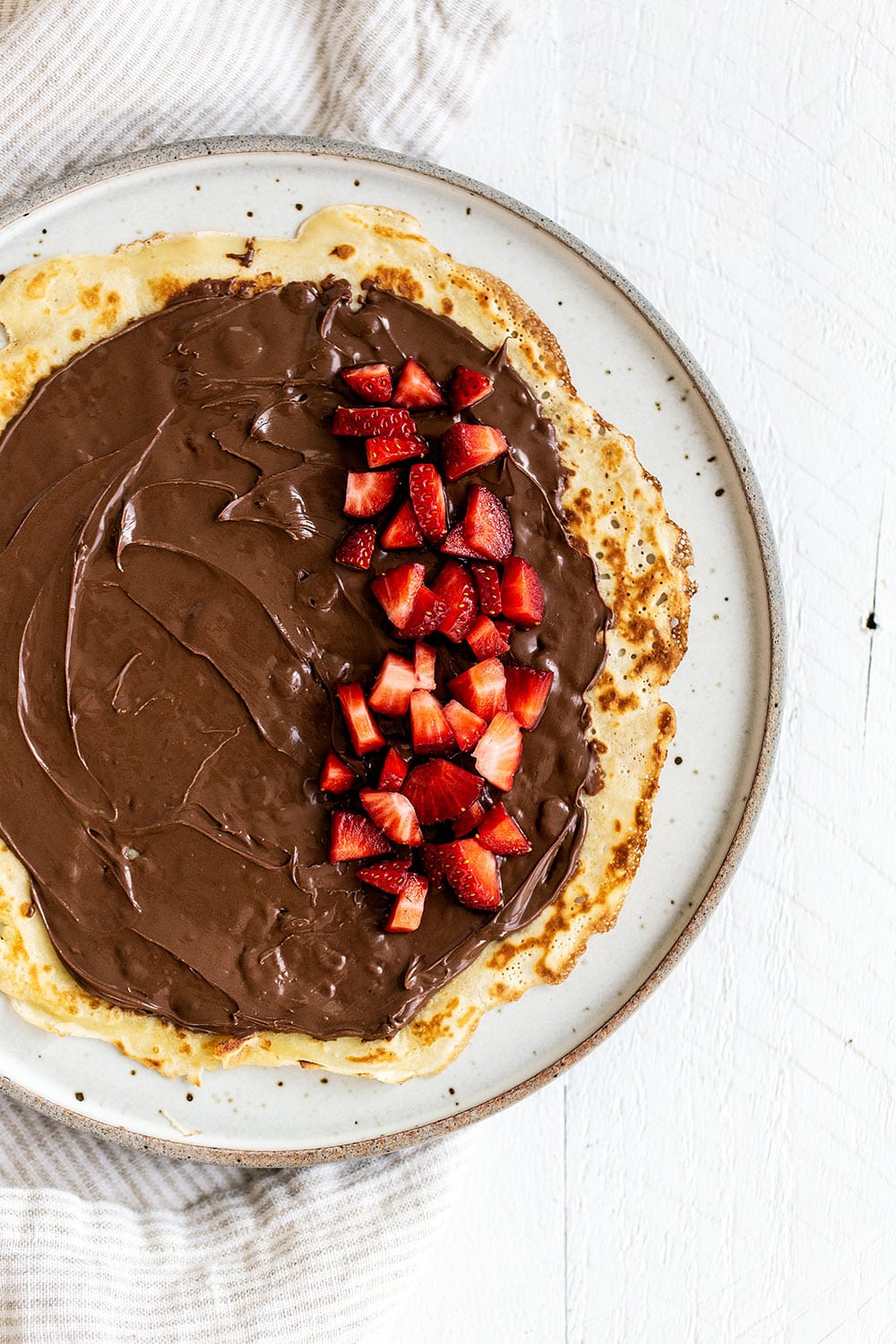 Open crepe on a plate with a generous spread of nutella and chopped strawberries