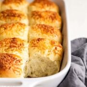 Garlic herb and cheese dinner rolls in a ceramic rectangular baking dish with one removed