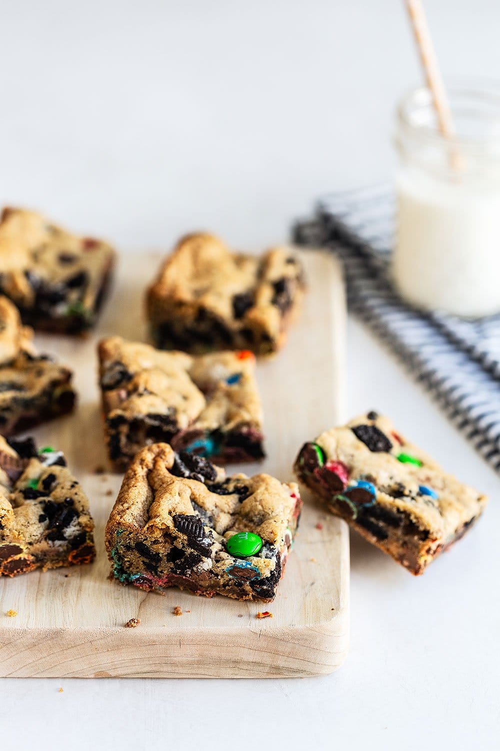 Loaded cookie bar squares on a cutting board with a glass of milk