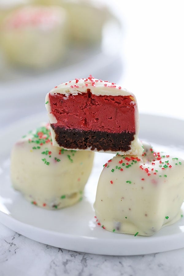 Red Velvet Cheesecake Bites feature squares of homemade red velvet cheesecake dipped in white chocolate and garnished with festive holiday sprinkles! Perfect Christmas treat.