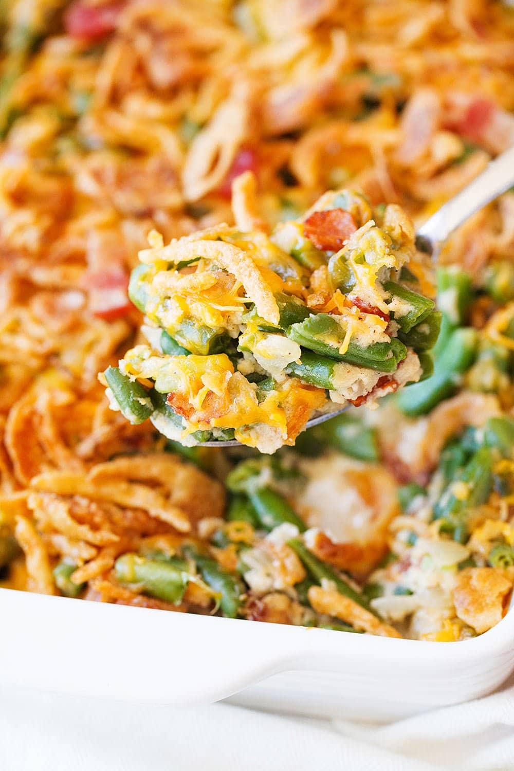 Scoop of cheesy green bean casserole with bacon in a white dish