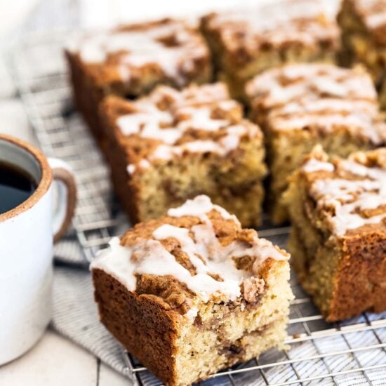 Multiple square pieces of coffee cake on a cooling rack near a cup of coffee