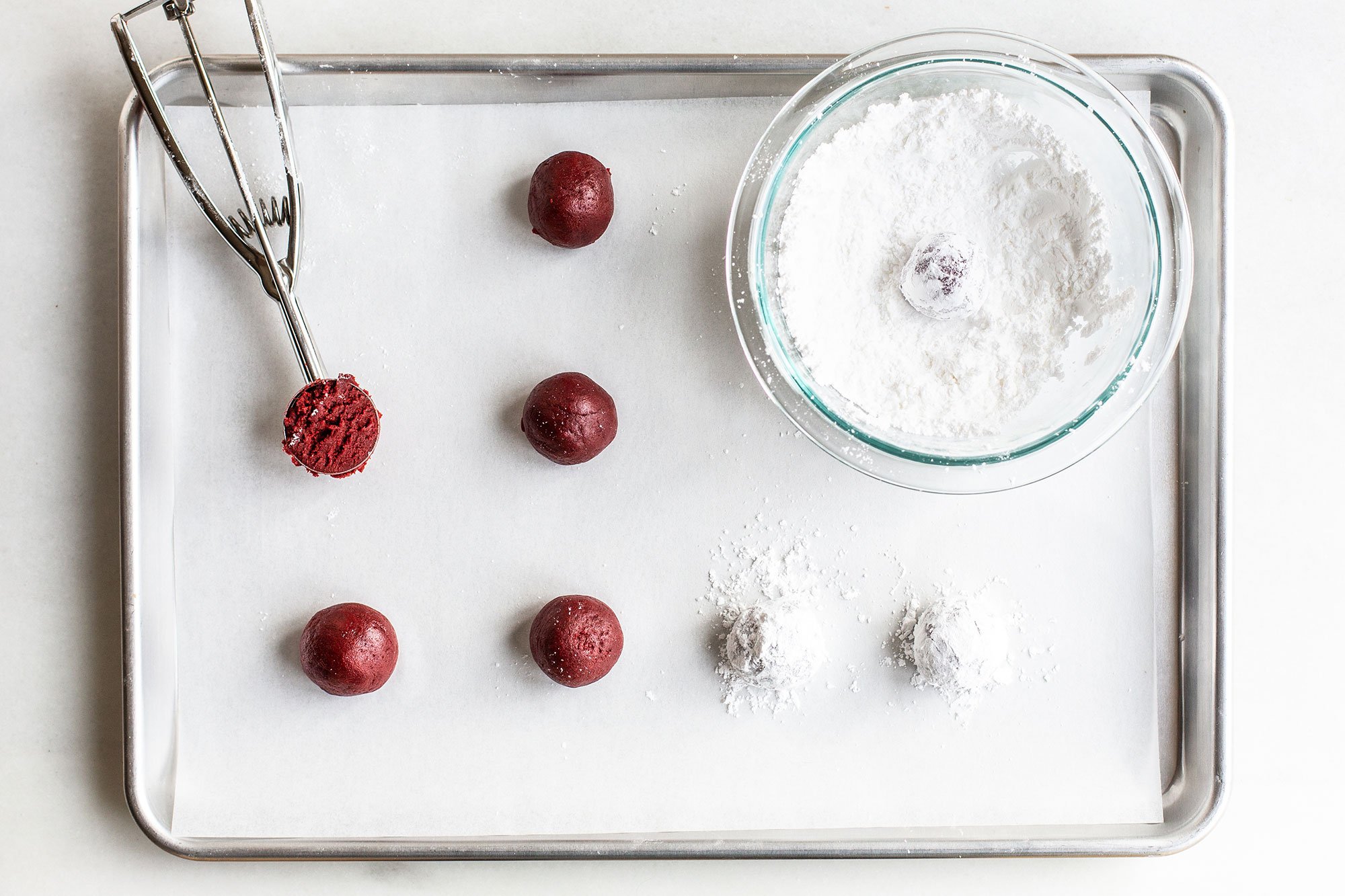 red velvet crinkle cookie dough rolled into balls and being coated in powdered sugar