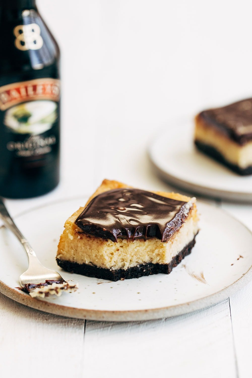 Bailey's cheesecake bar on a plate with a bottle of Bailey's Irish Cream