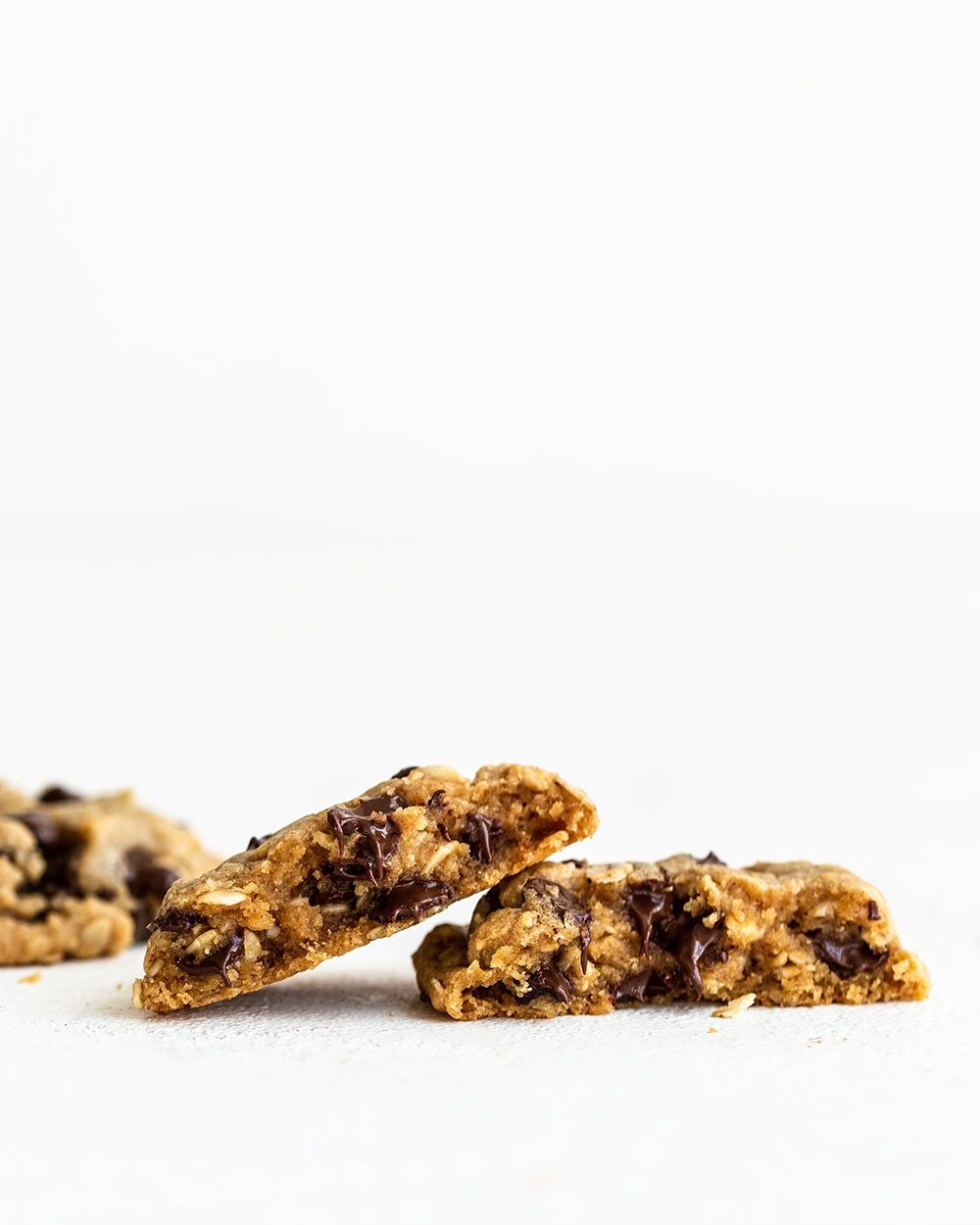 A peanut butter oatmeal chocolate chip cookie broken in half with a soft interior